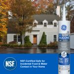 A white two-story house with dormer windows sits among autumn trees, with a GE silicone caulk tube in the foreground.