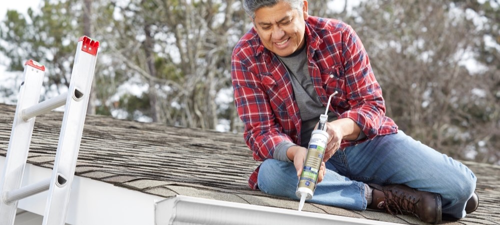 A homeowner applies gutter sealant to a metal gutter system.