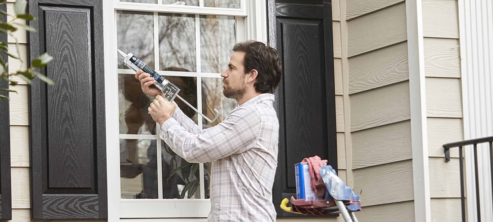 A contractor applying silicone sealant to a window frame.